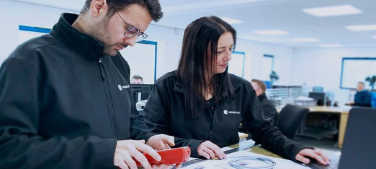 A woman and man looking at electronics wiring in a factory setting